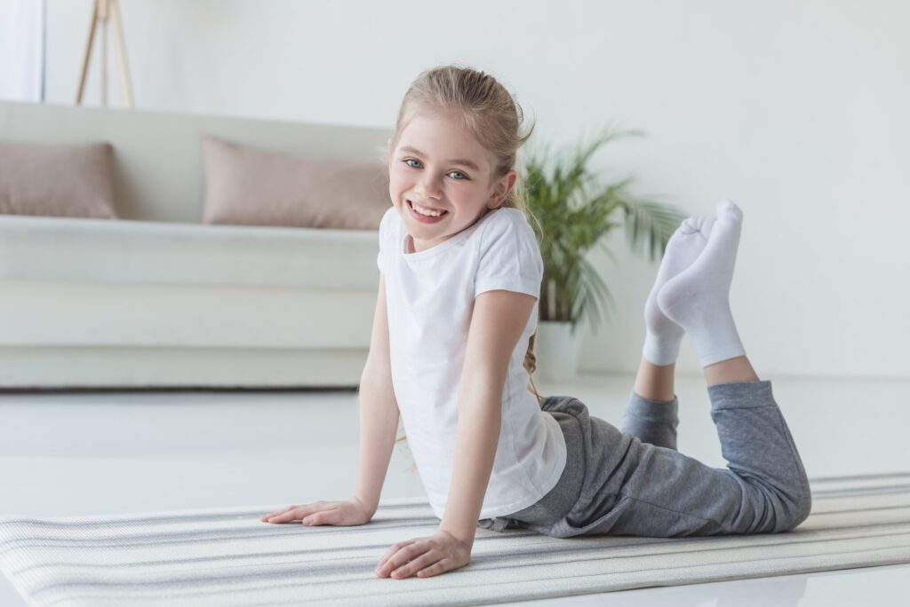 happy little child doing backbend on yoga mat and looking at camera
