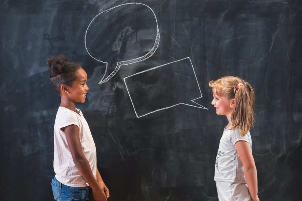 Two little girls having a debate in front of blackboard in classroom at school