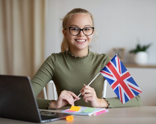 Smiling girl with flag of Great Britain using laptop